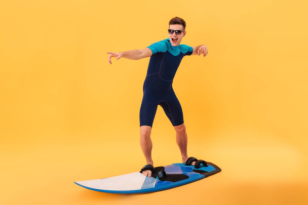 Image of happy surfer in wetsuit and sunglasses using surfboard - Foto, afbeelding
