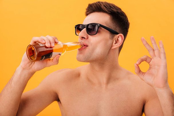 Close-up view of Smiling naked man in sunglasses drinking beer - Valokuva, kuva