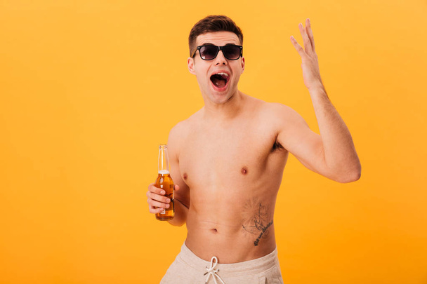 Happy screaming naked man in shorts and sunglasses holding beer - Foto, Bild