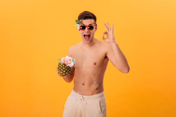 Happy naked man in shorts and unusual sunglasses holding cocktail - Fotó, kép