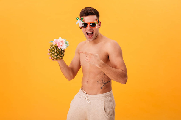 Cheerful naked man in shorts and unusual sunglasses holding cocktail - Foto, immagini