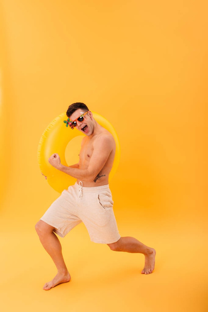 Full-length image of Cheerful naked man in shorts and sunglasses - Фото, изображение