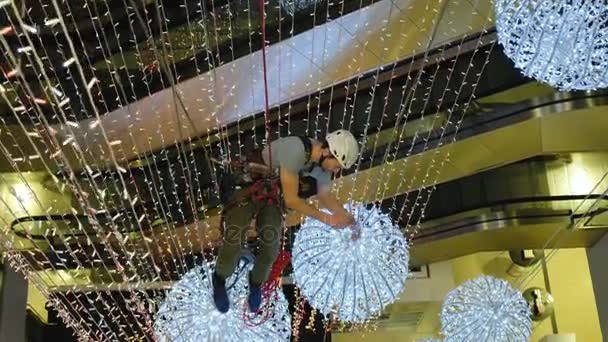 Industrial climber mounts Christmas decorations in the unsupported space in the shopping center - Footage, Video