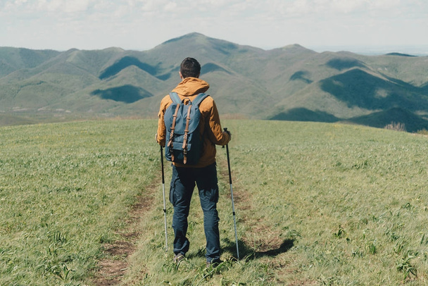 Explorer young man with backpack and trekking poles walking in the mountains - 写真・画像