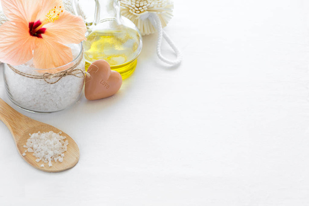 Wellness setting. Sea salt in glass, soap, towel, olive oil and flowers on white textured background. Space for copy. Flat lay - Photo, image