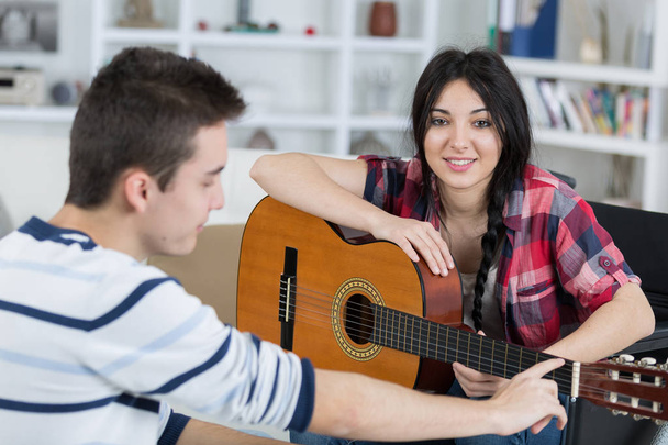 young man teaches his girlfriend to play the guitar indoors - Valokuva, kuva