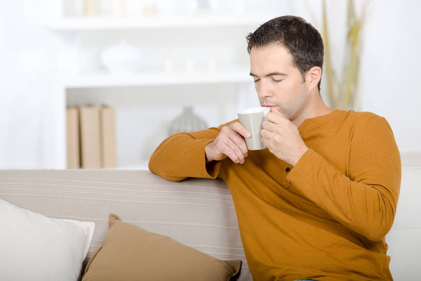 Man on sofa drinking from cup - Φωτογραφία, εικόνα