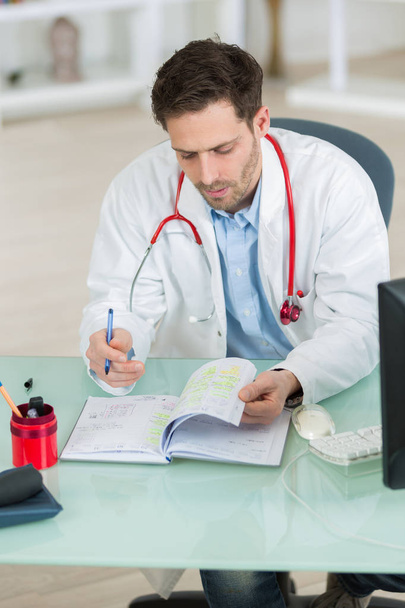 attractive young doctor writing prescription sitting at desk - Photo, image