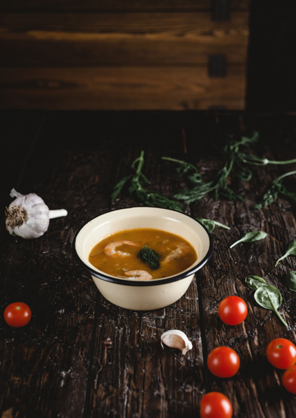 Суп с креветками в миске с помидорами и травами на деревянном столе
 - Фото, изображение