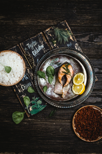Top view of baked salmon steak with lemon on rustic metal tray with rice side dish on dark wooden table - Фото, зображення
