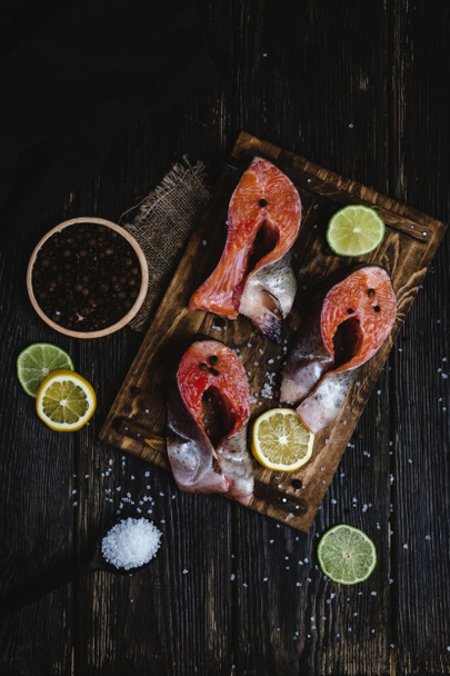 top view of fresh sliced red fish with spices and slices of citrus fruits on rustic wooden table - Foto, Imagem