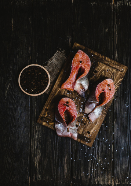 top view of sliced salmon fish on wooden cutting board with sackcloth, salt and peppercorns on rustic table   - Photo, Image