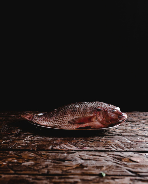 close-up view of fresh raw sea fish on vintage plate on rustic wooden table  - Фото, изображение