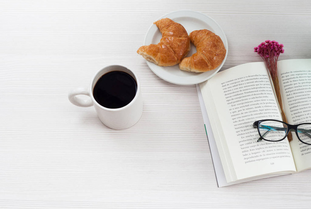 Büroschreibtisch von oben. Buch, Kaffee und Croissant auf weißem Tisch. - Foto, Bild