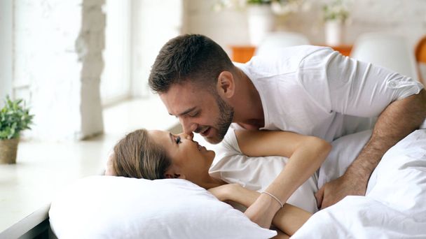 Young beautiful and loving couple wake up at the morning. Attractive man kiss and hug his wife in bed - Φωτογραφία, εικόνα
