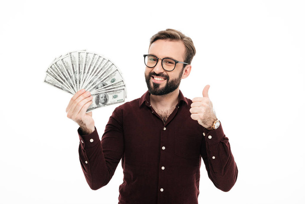 Smiling young man holding money showing thumbs up. - Фото, изображение