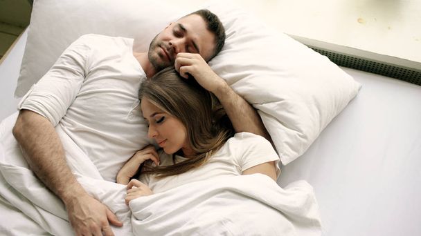 Young beautiful and loving couple kiss and hug into bed while waking up in the morning. Top view of attractive man kissing and talking his smiling wife - Foto, imagen