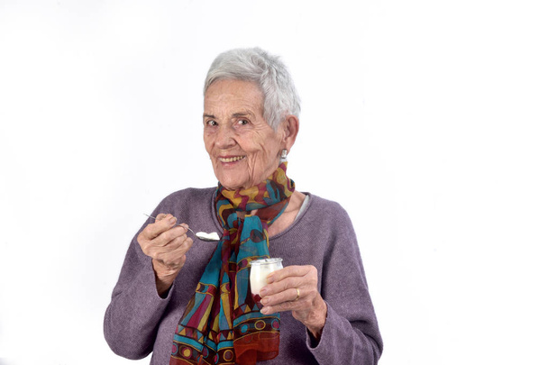 Ανώτερος γυναίκα τρώει γιαούρτι σε λευκό φόντο - Φωτογραφία, εικόνα