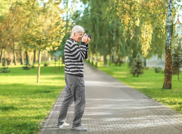 Stylish mature man taking photo in autumn park - Foto, afbeelding