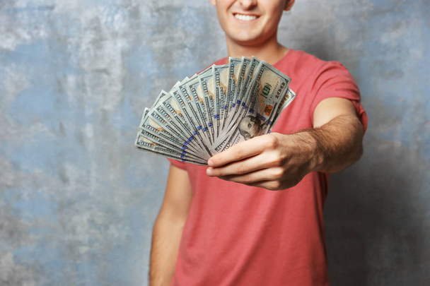 Young man holding money on grey background - Fotoğraf, Görsel