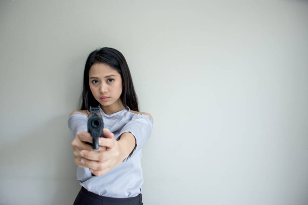 Портрет красивой азиатской молодой девушки, держащей черную пушку и стреляющей в камеру на белом фоне
. - Фото, изображение