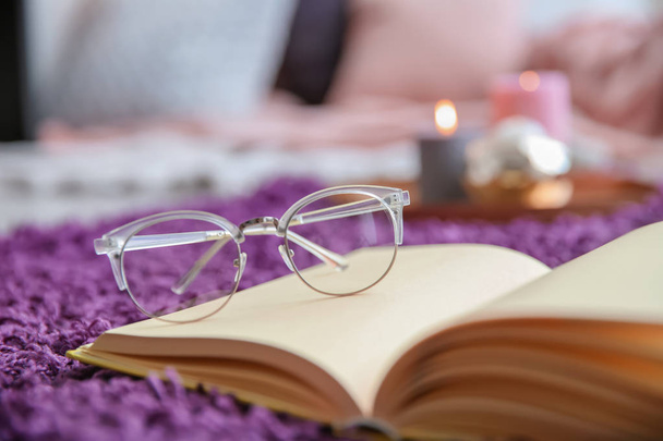 Open book with glasses on soft carpet, closeup - Foto, imagen