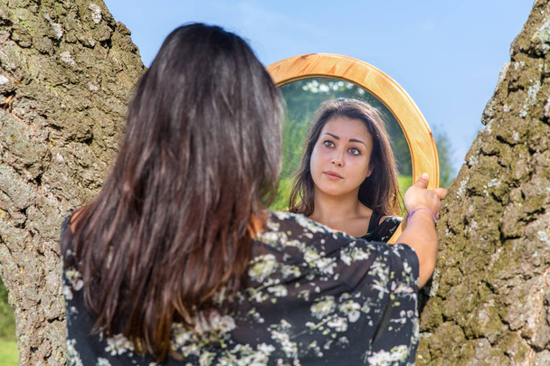 Frau blickt im Spiegel zwischen Bäumen - Foto, Bild