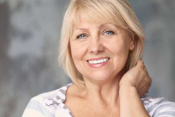 Portrait of beautiful mature woman on grey background - Фото, изображение