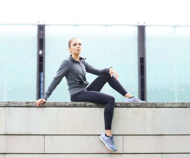 Young, fit and sporty woman sitting on concrete border. Fitness, sport, urban jogging and healthy lifestyle concept. - Фото, зображення