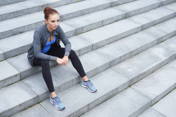 young, fit and sporty woman resting after training sitting on stairs. Fitness, sport, urban jogging and healthy lifestyle concept. - Фото, изображение