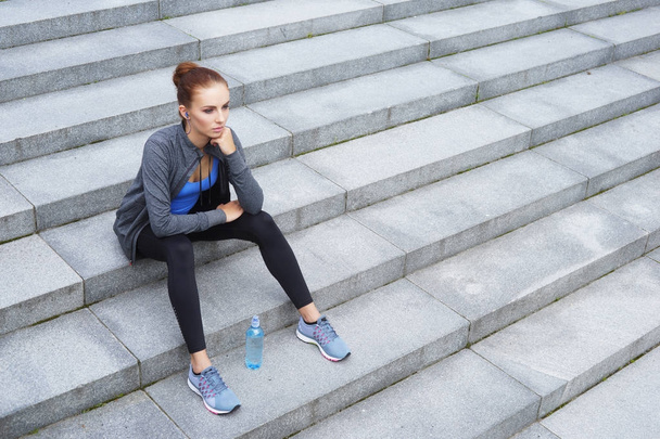 young, fit and sporty woman resting after training sitting on stairs. Fitness, sport, urban jogging and healthy lifestyle concept - Foto, afbeelding