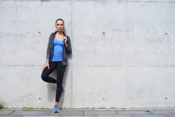 young, fit and sporty woman standing near concrete cement wall. Fitness, sport, urban jogging and healthy lifestyle concept - Fotó, kép