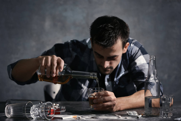 Man sitting at table and pouring whiskey into glass. Alcoholism concept - Фото, зображення