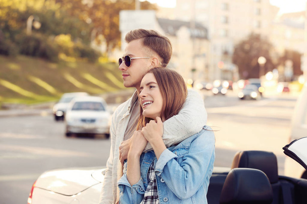 Happy young couple standing near modern car outdoors - Photo, image
