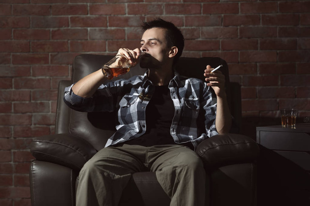 Man drinking whiskey and smoking cigarette in armchair. Alcoholism concept - Foto, Imagem