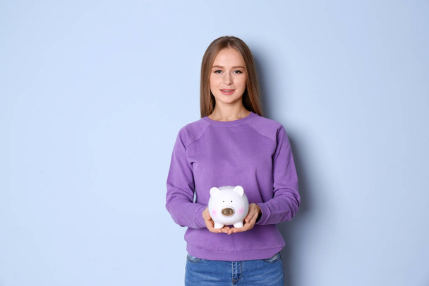 Young woman holding piggy bank on color background - Фото, зображення