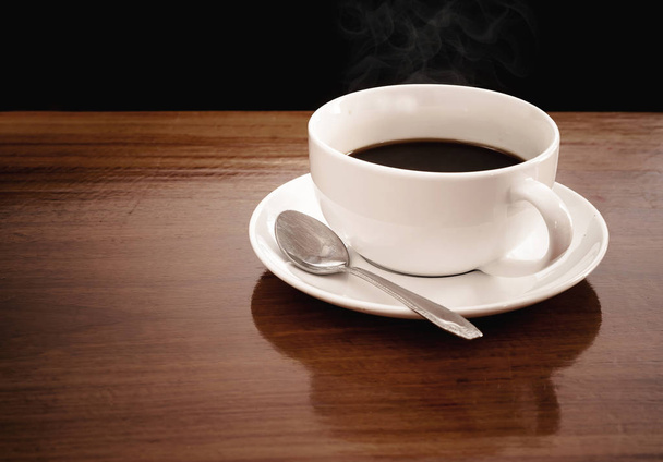 A cup of coffee is placed on a wooden table. The background is black. - Fotografie, Obrázek