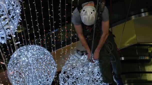Průmyslový lezec připojí vánoční ozdoby v nepodporované prostoru v nákupním centru - Záběry, video