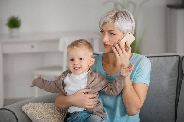 Young mother talking on phone while holding her baby at home - Foto, Bild