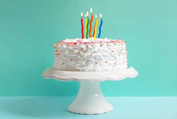 Stand with birthday cake and candles on table against color wall - Foto, imagen