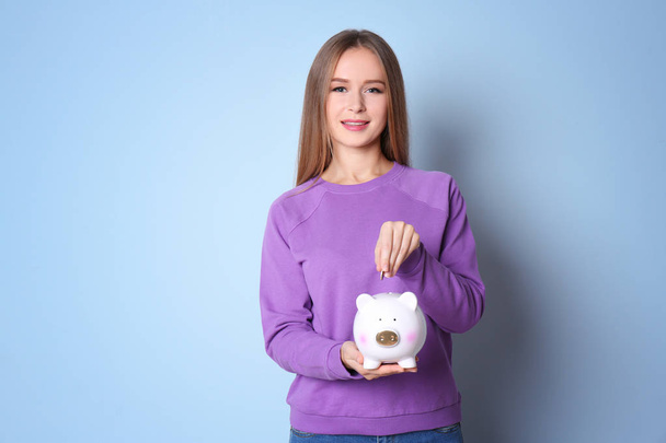 Young woman putting coin into piggy bank on color background - Foto, imagen