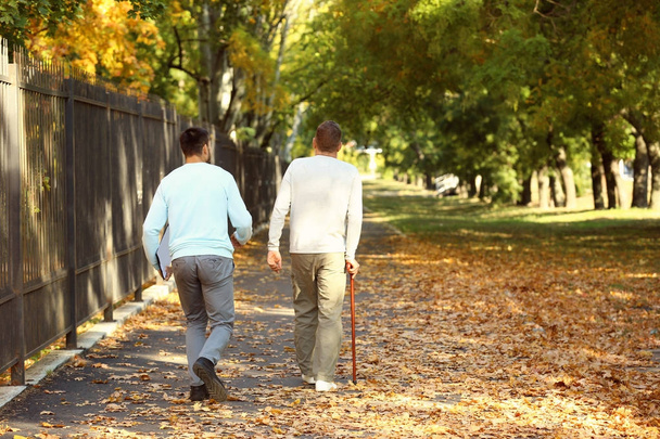 Молодой сиделка гуляет со старшим мужчиной в парке
 - Фото, изображение