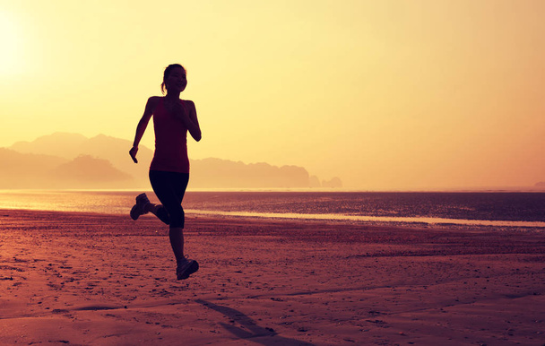 Young fitness woman running on sandy beach during sunrise  - Fotó, kép