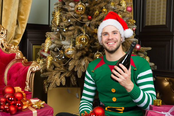 Mann mit Weihnachtsmannhut lächelt mit Champagnerflasche - Foto, Bild
