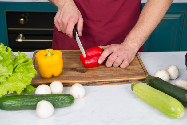 Hands cut red pepper with knife on wooden cutting board - Φωτογραφία, εικόνα