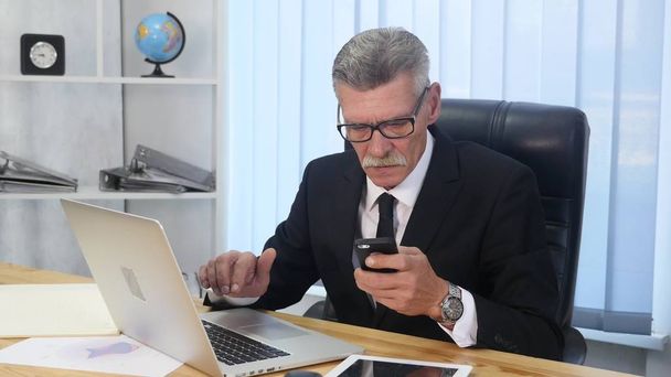 Senior man speaks with white smartphone in office - Foto, imagen