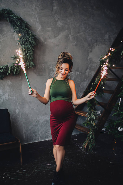 kaukasische schwangere Frau mit Make-up und lockigem Haar hält funkelndes Feuerwerk, Porträt der zukünftigen Mutter, glückliche Schwangerschaft, Modeporträt, stilvolle Schwangerschaft - Foto, Bild