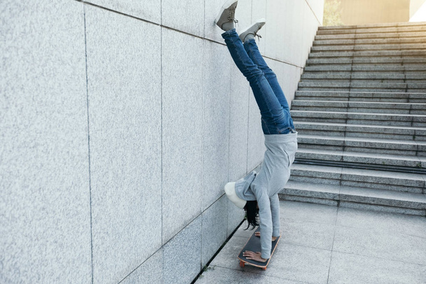 female skateboarder doing a handstand on skateboard against wall - Foto, Bild
