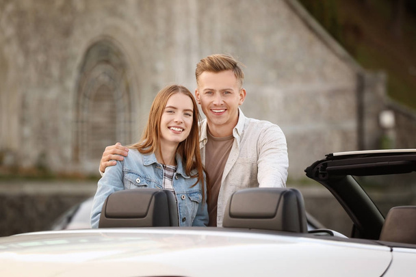 Happy young couple standing near modern car outdoors - 写真・画像