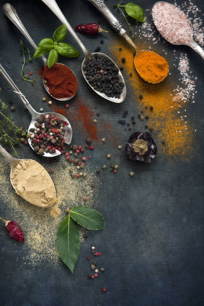 close-up of colored spices in metal spoons on black table background - 写真・画像